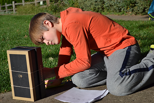 A student takes a reading on one of the thermometers on his sling psychrometer.